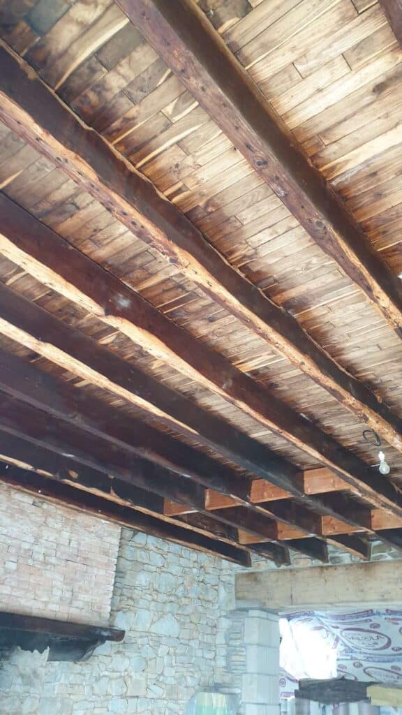 Solives anciennes bûchées et brossées avant traitement bois, sous un plafond en lambris, dans une maison en pierre près de Rennes