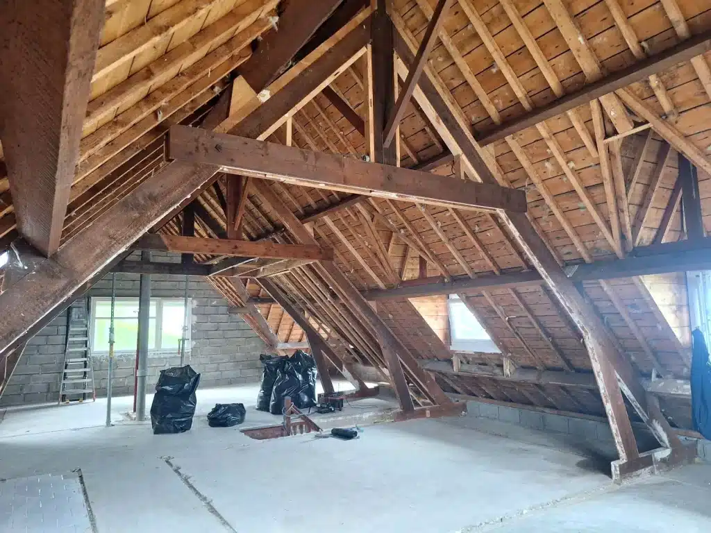 Vue d'ensemble d'une charpente traditionnelle en bois dans des combles, lors d'un chantier de traitement du bois à Lannion.