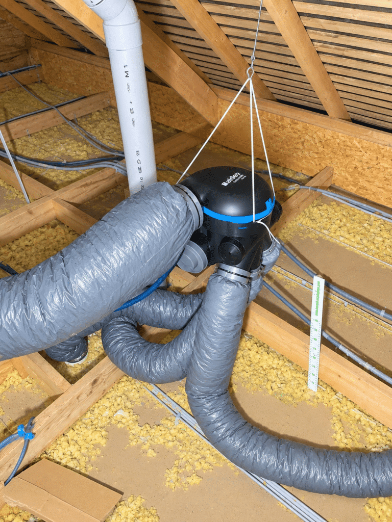 Caisson de VMC simple flux Aldes suspendu dans les combles isolés, raccordé à des gaines isolées, dans une maison du secteur rennais